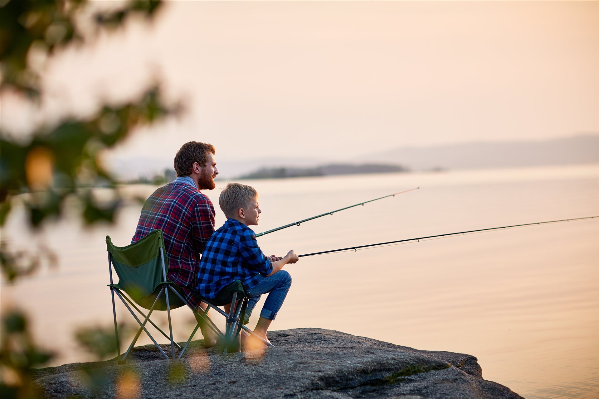A father and son fishing from a rock at sunset